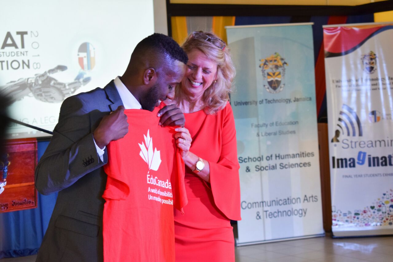 Picture 1: Archibald Gordon receiving an “EduCanada” T-shirt from Her Excellency, Canadian High Commissioner to Jamaica Laurie Peters at the launch of the final year student exhibition of the BA Communication Arts and Technology programme at the Papine campus of the University of Technology, Jamaica on May 3 2018.